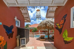 A covered outdoor area with a pool, a thatched roof, and butterfly murals on the walls. - Studio Sun by Casa Lou Lou- modern  with shared pool- central location (Noord)