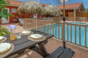 Ein Poolbereich mit Esstisch, Grill und Strohdachschirmen.