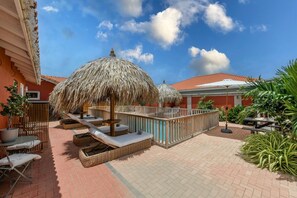 Un patio con sombrillas de paja, sillas de descanso y una zona de piscina.