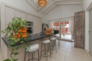 A kitchen with a central island, bar stools, a potted plant, and a view through a glass door. - Casa Lou Lou Beachhouse 2bdr 2Bth shared pool - central location (Tanki Leendert)