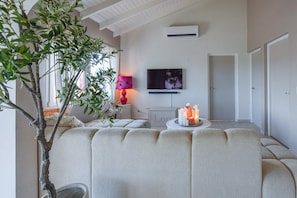 A living room with a sofa, a television, a plant, and a table with candles. - Casa Lou Lou Beachhouse 2bdr 2Bth shared pool - central location (Tanki Leendert)