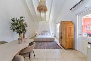 A bedroom with a bed, a bedside table, a chair, a wardrobe, a plant, and a hanging light fixture. - Studio Palm by Casa Lou Lou- modern  with shared pool- central location (Noord)