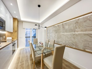 A modern kitchen with a built-in microwave, wooden cabinets, and a glass dining table with chairs. - 2BR/2BA Apartment Next to Gran Vía Berlany España (Madrid)