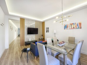 A modern dining area with a glass table, white chairs, and a TV mounted on the wall. - Spacious 2BR/2BA Close Plaza España Berlany España (Madrid)