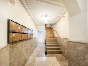 A hallway with a marble floor, wooden lockers on the left, and a wooden staircase with a handrail on the right. - Spacious 2BR/2BA Close Plaza España Berlany España (Madrid)