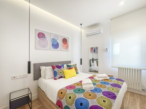 A modern bedroom with a bed, colorful bedding, a bedside table, a mirror, and artwork on the wall. - Spacious 2BR/2BA Close Plaza España Berlany España (Madrid)