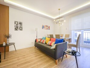 A modern living room with a sofa, a coffee table, and a dining area with chairs. - Spacious 2BR/2BA Close Plaza España Berlany España (Madrid)
