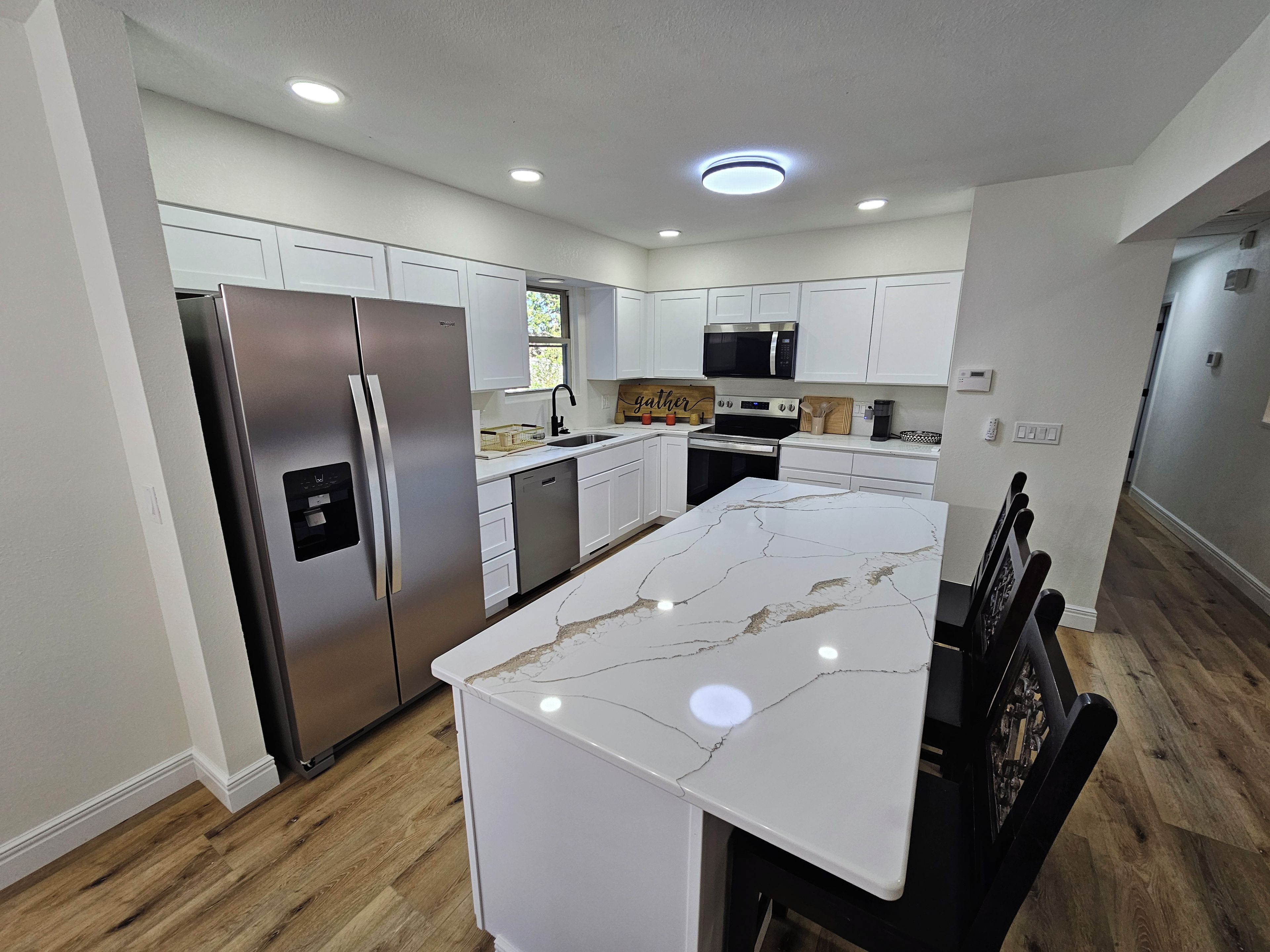A modern kitchen with white cabinetry, stainless steel appliances, and a marble island.