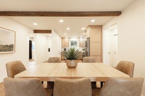 Ein Esszimmer mit Holztisch und -stühlen, einem Blumentopf und einer Küche im Hintergrund.