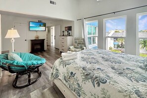 Quarto com cama, poltrona, televisão, lareira e vista para o exterior.