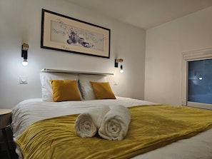 Una habitación de hotel con cama, dos almohadas, una obra de arte enmarcada, apliques de pared y una ventana.