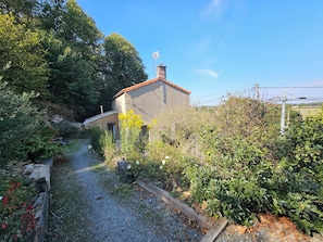 Una casa de campo con camino de grava, rodeada de vegetación exuberante y un cielo despejado.
