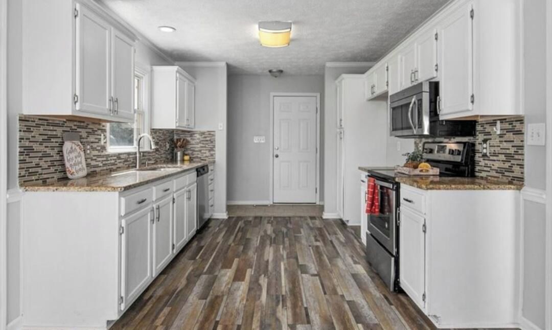 Una cocina con armarios blancos, suelo de madera, microondas y un lavamanos.