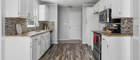 Una cocina con armarios blancos, suelo de madera, microondas y un lavamanos.