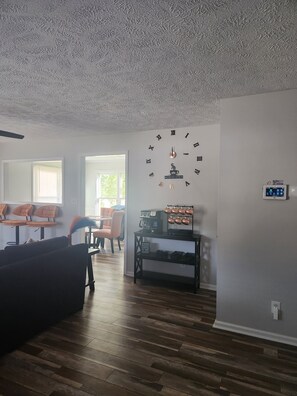 Ein Wohnzimmer mit einer Uhr an der Wand, einer Kaffeemaschine und einem Schild mit der Aufschrift 'Kaffee gibt es immer'.