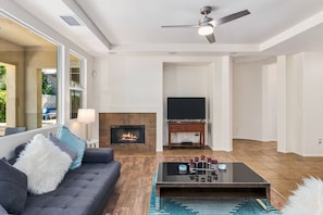 A modern living room with a fireplace, a television, and a sofa with decorative pillows. - For Shore | Private Pool & Spa | Fire pit | Rancho Mirage (Rancho Mirage)