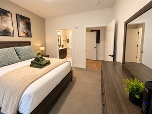 A hotel room with a bed, a bedside table, a mirror, a plant, and a door leading to another room. - Downtown Cincinnati | Free Parking, Pool & Gym (Cincinnati)