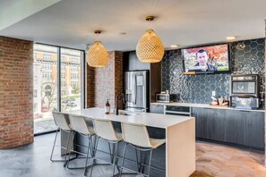 A modern kitchen with a large island, bar stools, a TV, and a city view. - Downtown Cincinnati | Free Parking, Pool & Gym (Cincinnati)