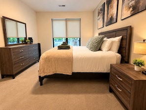 A bedroom with a bed, a dresser, a nightstand, and a window with blinds. - Downtown Cincinnati | Free Parking, Pool & Gym (Cincinnati)