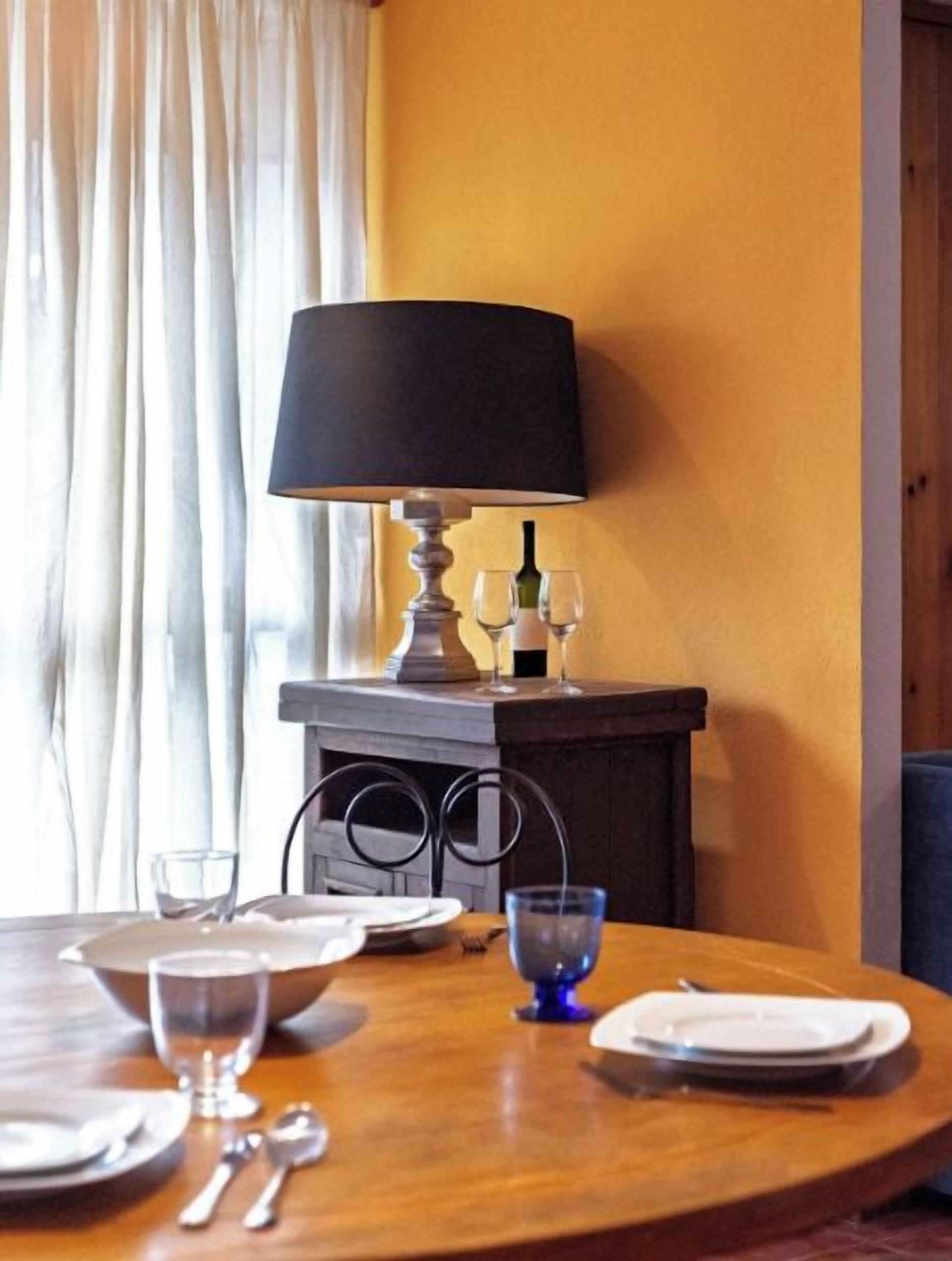 Ein Esstisch, gedeckt mit Tellern, Gläsern und Besteck, eine Lampe und eine Weinflasche auf einem Tisch.