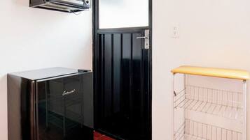 Eine kleine Küche mit integriertem Mikrowellenherd, einem Kühlschrank und einem weißen Drahtregal.