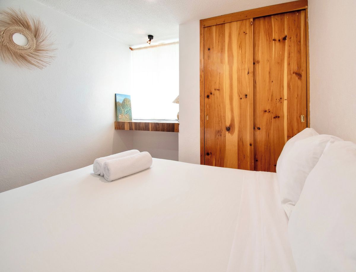 A hotel room with a bed, a wooden wardrobe, and a painting on the wall.