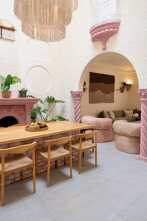 Un intérieur chaleureux avec une table à manger en bois, des chaises, un canapé rose et une cheminée.