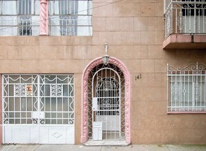 A building facade with a pink archway entrance, barred windows, and a balcony with decorative railings. - Casa Raíz| A Place to Belong, Rooted in Connection (Mexico City)