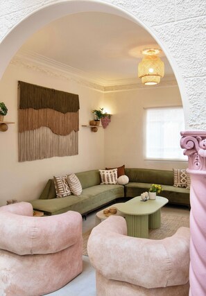 A living room with a green sofa, pink armchairs, a round coffee table, and a large wall hanging. - Casa Raíz| A Place to Belong, Rooted in Connection (Mexico City)
