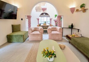 A modern living room with a green sofa, two pink armchairs, a green ottoman, and a coffee table with flowers. - Casa Raíz| A Place to Belong, Rooted in Connection (Mexico City)