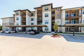 A multi-story residential building with a covered parking area, multiple balconies, and a landscaped front yard. - Blueground | Scofield Farms, pool, nr Walnut Creek (Austin)