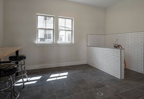 A bathroom with two windows, a white tiled shower area, and a bar stool. - Blueground | Scofield Farms, pool, nr Walnut Creek (Austin)