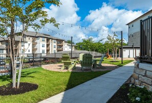 A residential area with a grassy lawn, a playground with green play equipment, and a building with balconies. - Blueground | Scofield Farms, pool, nr Walnut Creek (Austin)