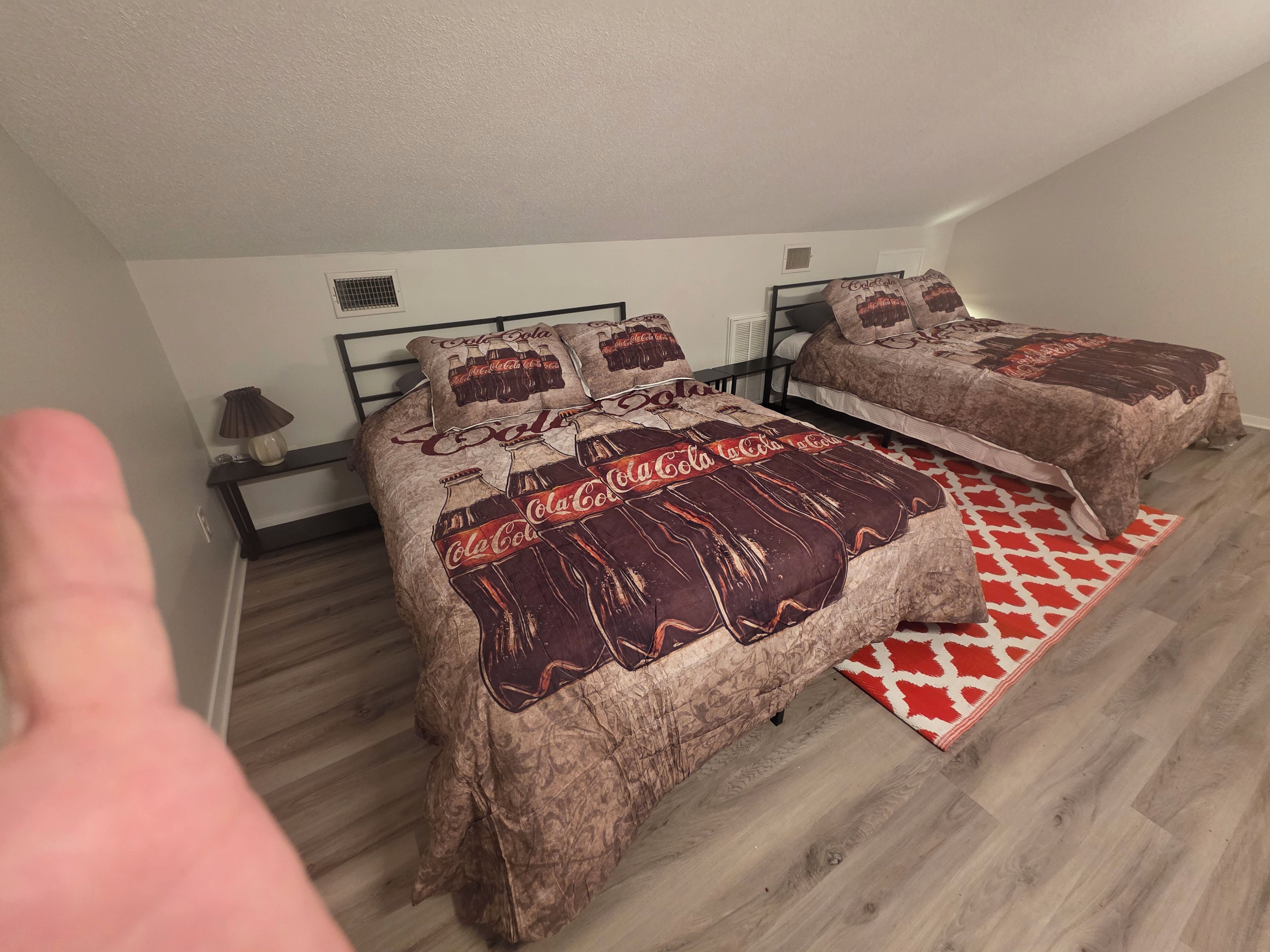 Un dormitorio con dos camas, un tapete rojo y blanco estampado, y un calentador de pared.