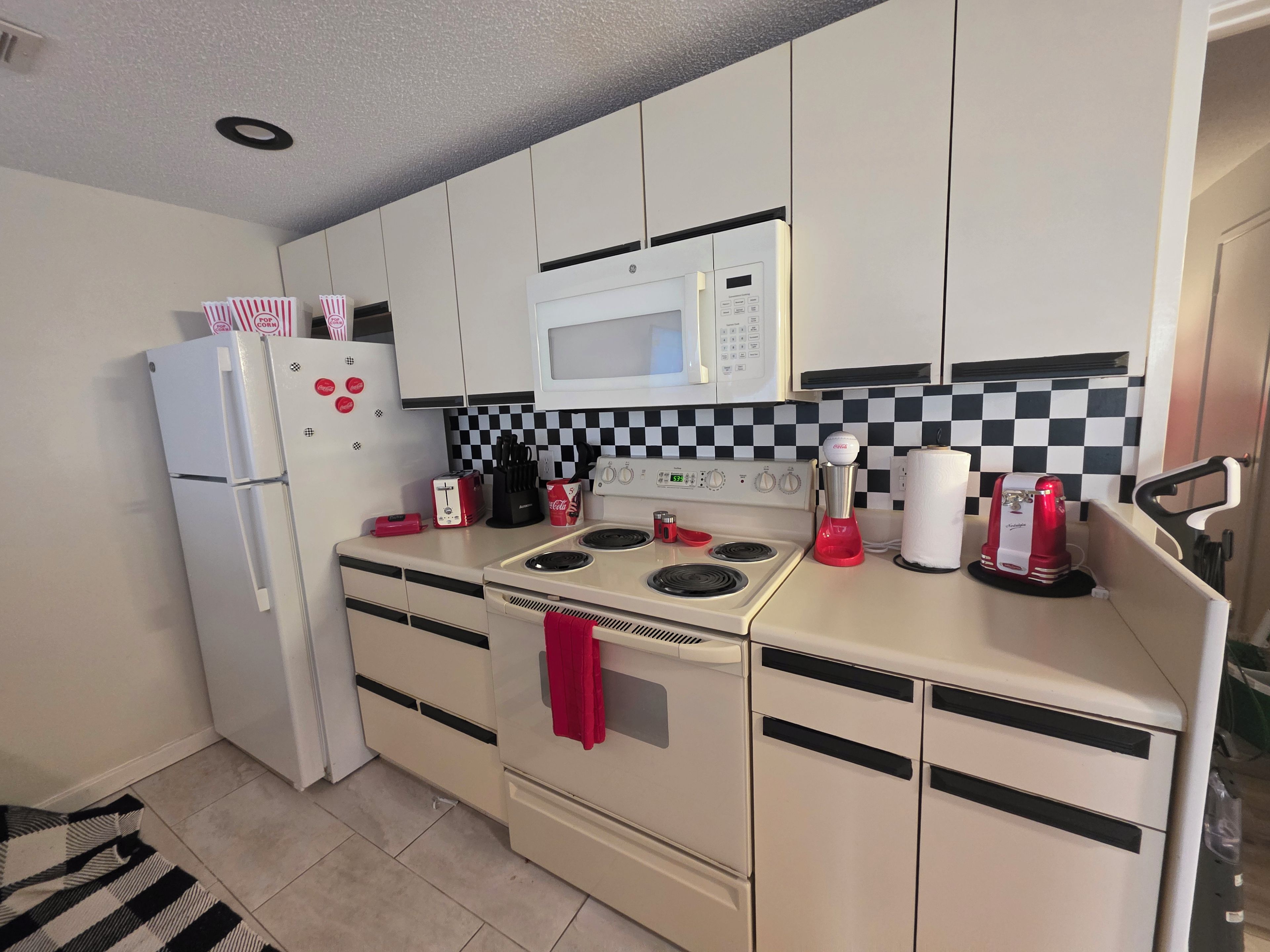 A compact kitchen with a refrigerator, microwave, stove, and various appliances.