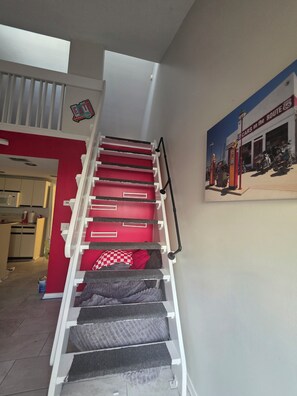 Eine Treppe mit roten Stufen und einem weißen Geländer, die zu einem Raum mit einer Küche im Hintergrund führt.