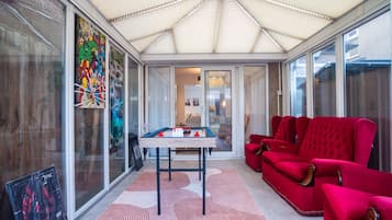 Une véranda équipée d’une table de billard, de canapés rouges et d’une grande fenêtre ornée d’œuvres d’art.