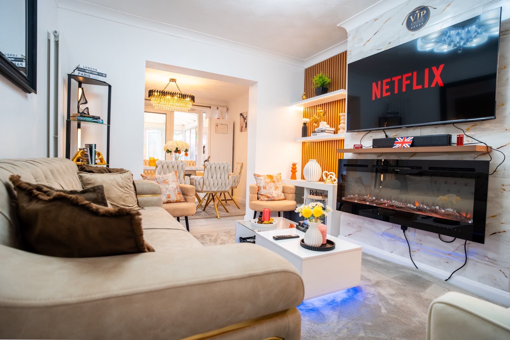 A modern living room with a beige sofa, a fireplace, a flat-screen TV, and a bookshelf.