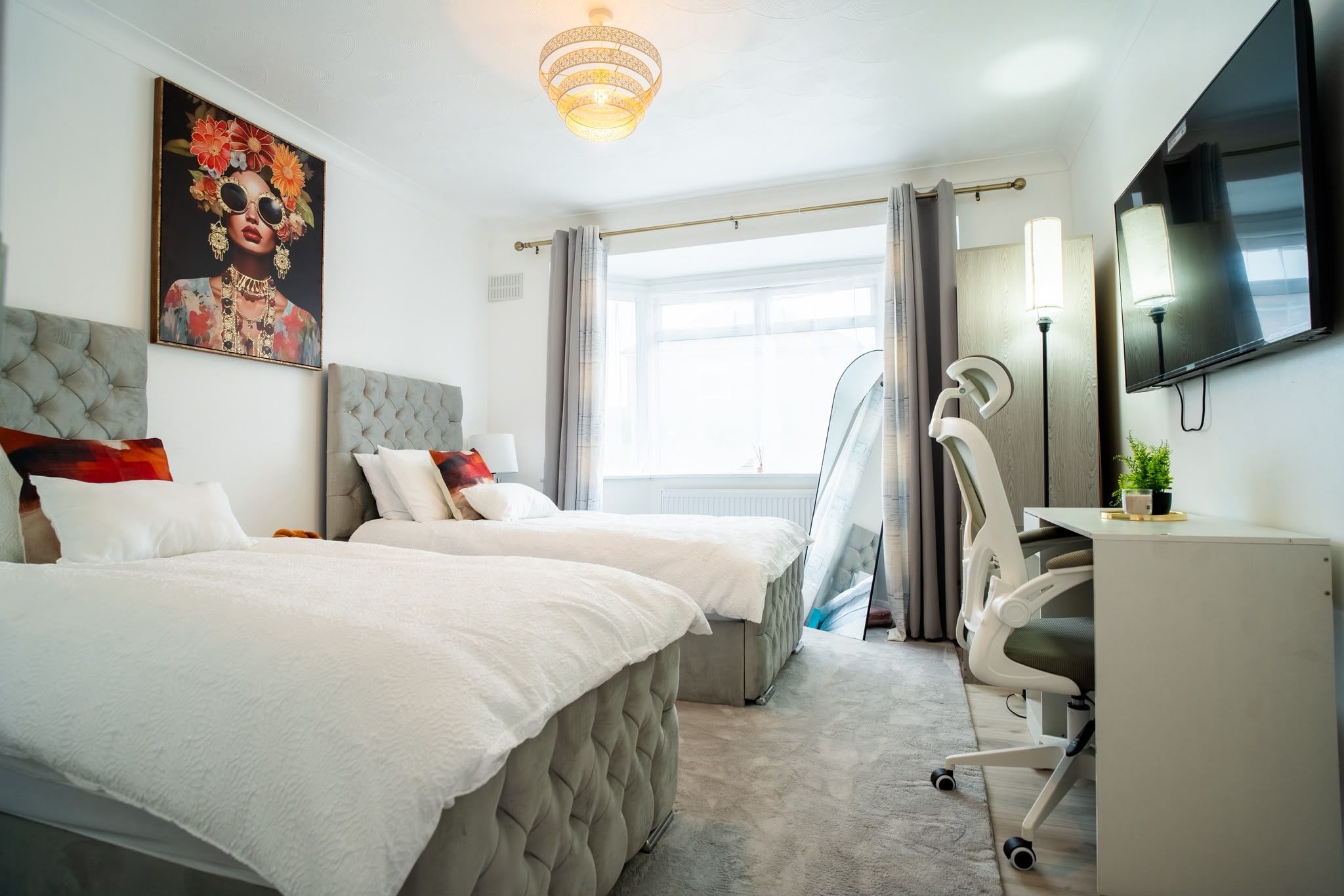 A hotel room with two beds, a desk, a chair, a TV, and a large window with curtains.