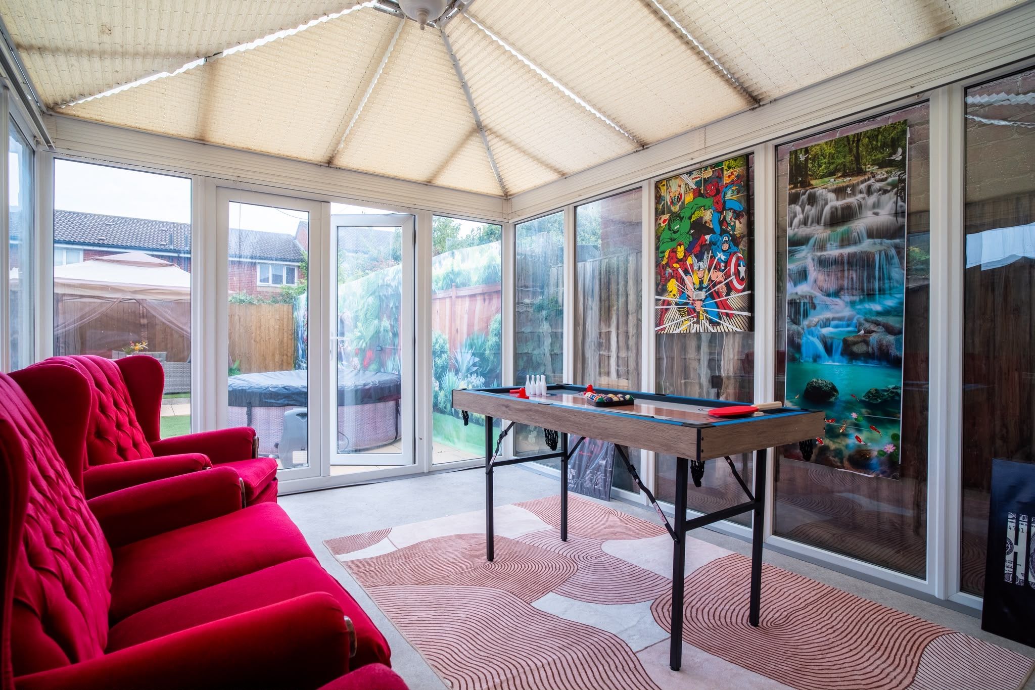 A sunroom with a pool table, red chairs, and large windows with artwork.