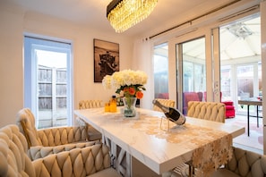 A dining area with a marble table, cushioned chairs, a chandelier, and a vase with flowers.