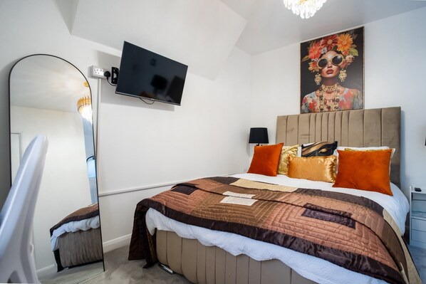 A bedroom with a bed, a television mounted on the wall, a mirror, and a painting.