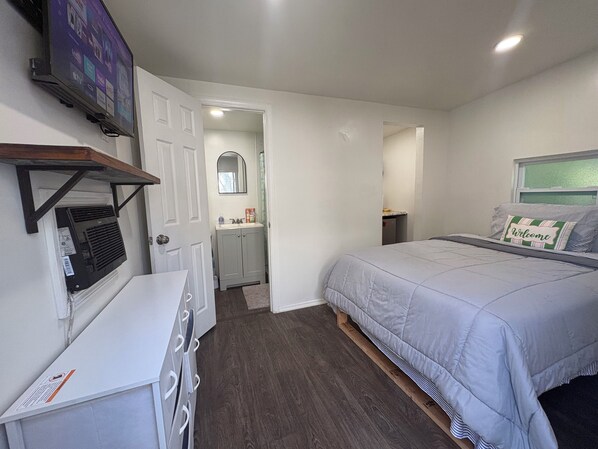 A bedroom with a bed, a dresser, a television, and a bathroom visible through an open door.