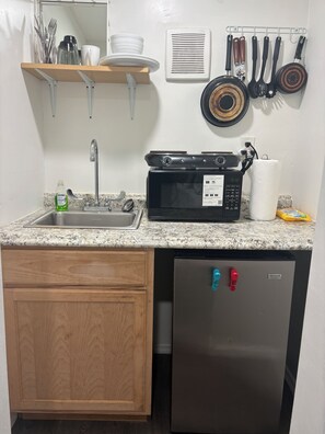 A kitchen with a stainless steel refrigerator, a microwave, a sink, and a wooden cabinet.