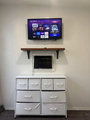 A television mounted on a wall above a white dresser with drawers.
