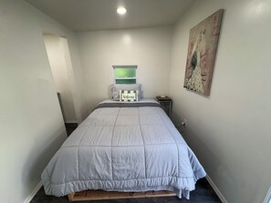 A neatly made bed with a striped pillow and a welcome sign, a small bedside table with a phone, and a wall painting.