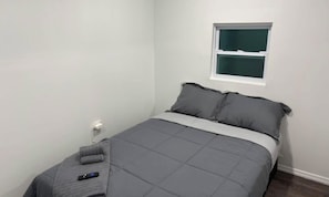 A bedroom with a bed, pillows, a remote control, and a window.