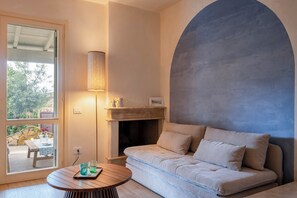 Een gezellige woonkamer met een bank, een open haard, een tafel met glazen en uitzicht door een glazen deur.