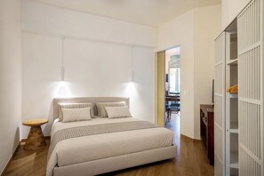 Een slaapkamer met een bed, nachtkastjes, een kledingkast en uitzicht op een andere kamer.