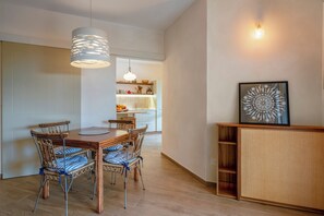 A dining area with a wooden table and wicker chairs, a kitchen in the background, and a wall-mounted light fixture. - Villa Tigli: A 5-Minute Walk From the Beach by Top Villas Sardinia (Quartu Sant'Elena)